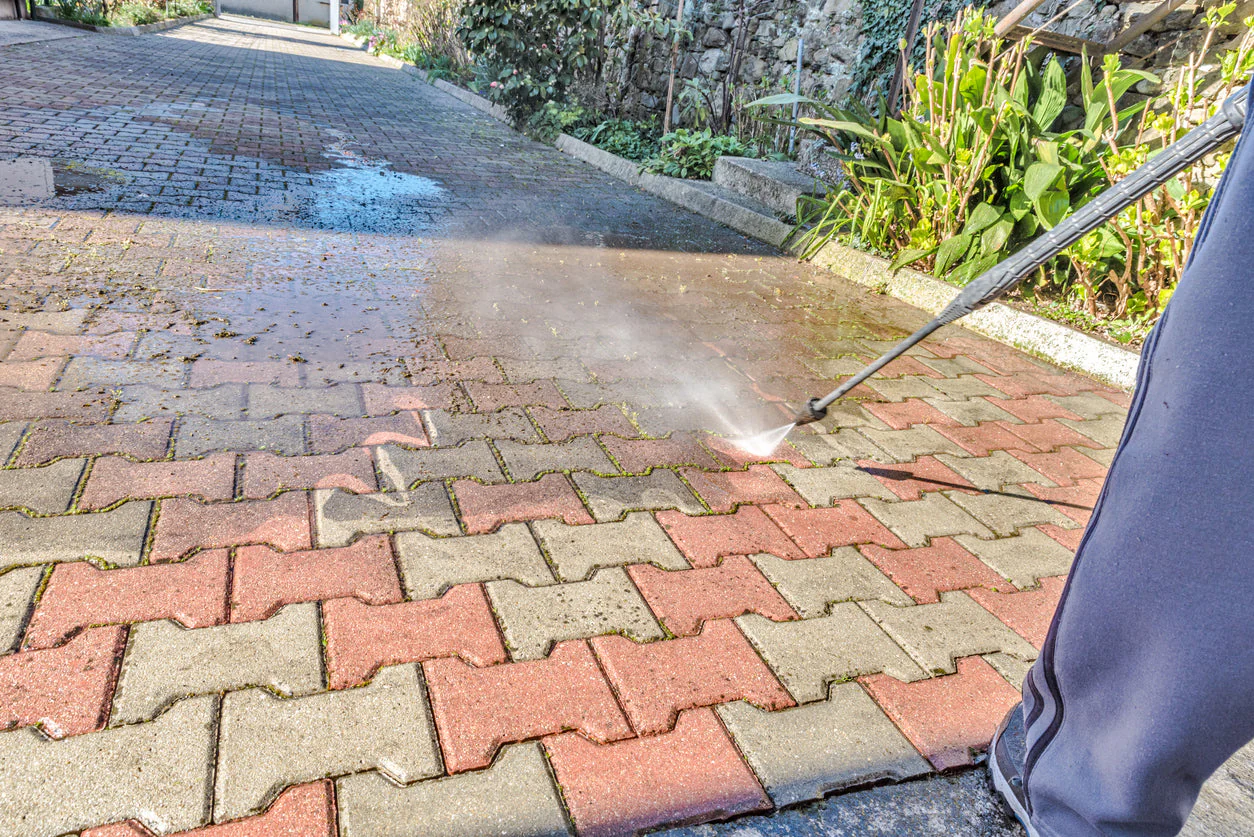 Technician pressure washing a brick paver driveway to remove moss, algae, and surface stains in Massachusetts.